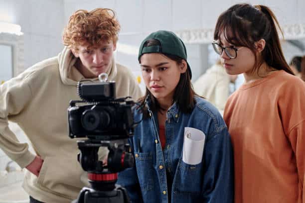 Group of young adults collaborating on creative project in indoor setting, involving filming process with professional camera equipment
