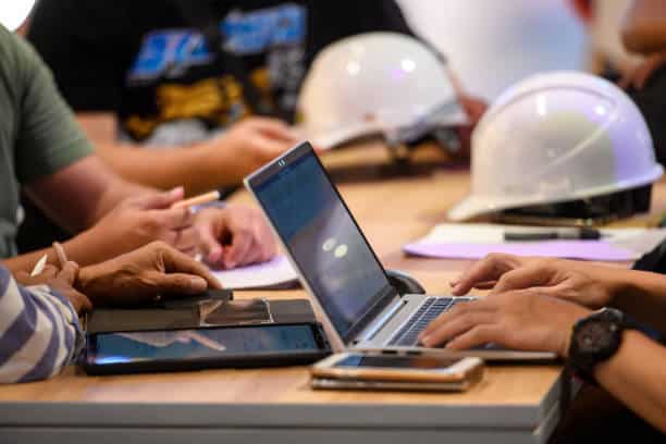 Meeting of project employees, architects, construction workers, contractors, company owners, all sitting at the table, discussing, agreeing, using laptop